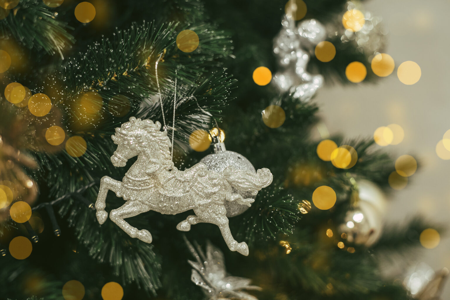 Christmas tree with silver horse toy. Holiday background with bokeh lights. Copy space
